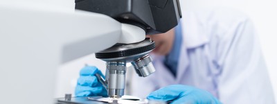 Scientist in a lab coat and gloves looking through a microscope